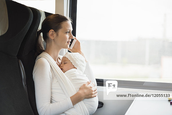 Mother with baby girl traveling by train talking on cell phone