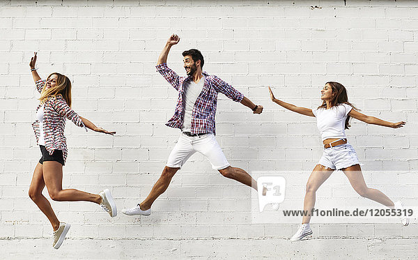 Three friends jumping mid-air in front of white wall