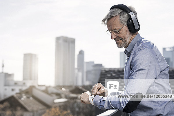 Grauhaariger Geschäftsmann mit Kopfhörern auf smartwatch