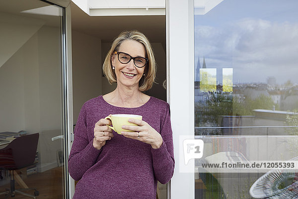 Porträt einer lächelnden reifen Frau mit Kaffeetasse auf dem Balkon