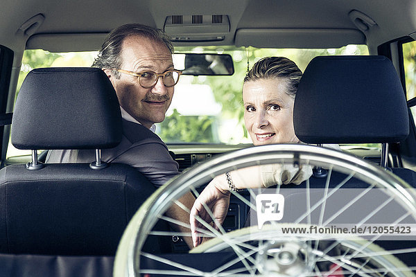Lächelndes Paar im Auto mit Rollstuhl im Kofferraum