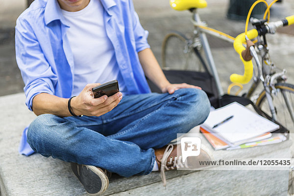 Young man with racing cycle sitting on bench using cell phone