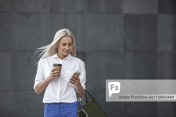 Lächelnde Geschäftsfrau mit Kaffee zum Mitnehmen und Handy unterwegs