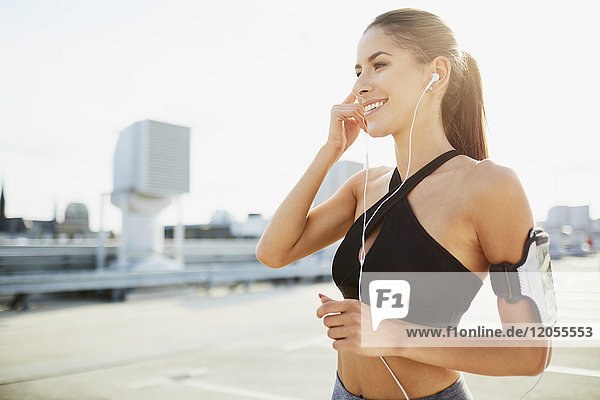 Smiling young woman wearing earphones preparing to work out in the city