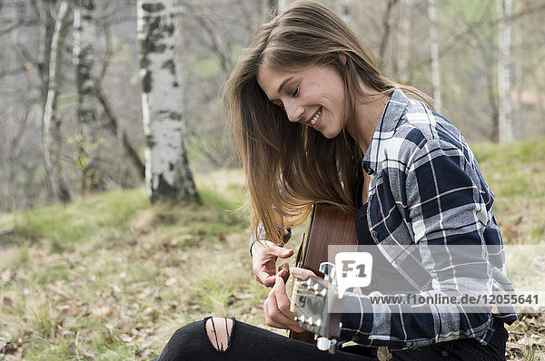 Lächelnde Frau spielt Gitarre im Wald