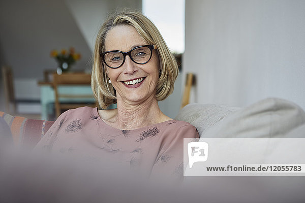 Porträt der lächelnden reifen Frau zu Hause auf dem Sofa