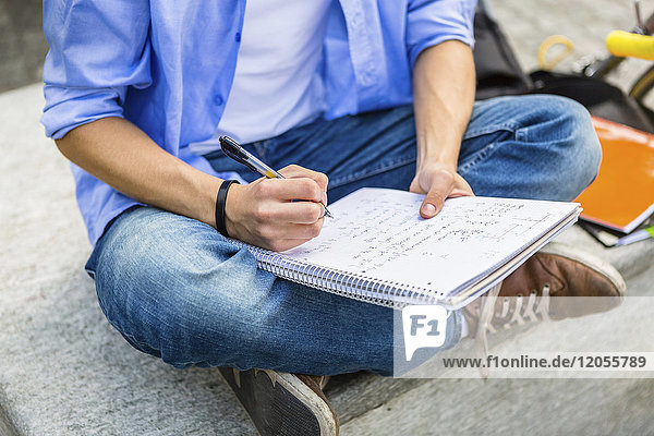 Junger Mann sitzt auf der Bank und schreibt auf Notizblock  Teilansicht