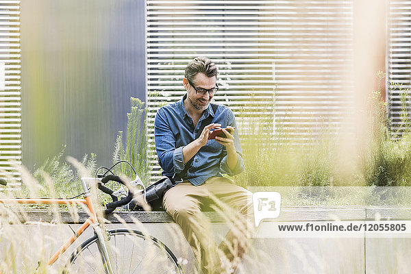 Lächelnder Geschäftsmann mit Handy neben dem Fahrrad