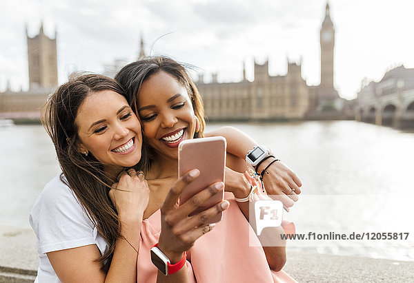 UK  London  two happy women with smartphone near Westminster Bridge