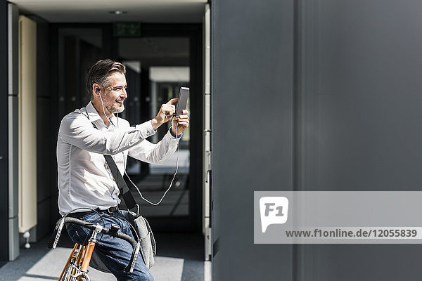 Businessman with bicycle in office passageway using cell phone
