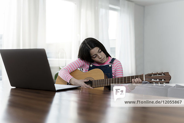 Girl playing guitar in front of laptop