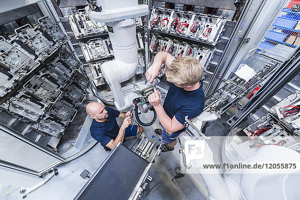 Two colleagues working at industrial robot in modern factory