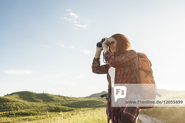 Teenage girl with backpack using binoculars in nature