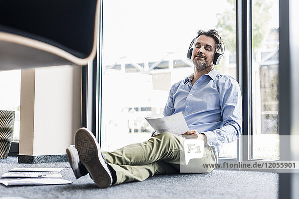 Geschäftsmann mit Kopfhörer im Büro auf dem Boden sitzend