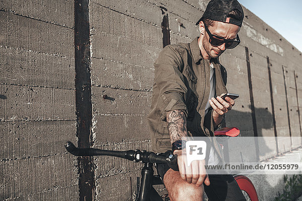 Junger Mann mit Handy auf Fixie Bike