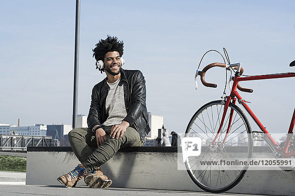 Smiling man listening to music on headphones next to his bicycle