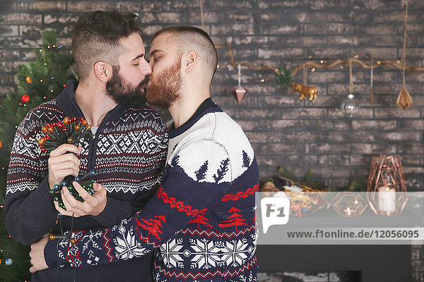 Kussendes schwules Paar mit Lichterkette zur Weihnachtszeit zu Hause