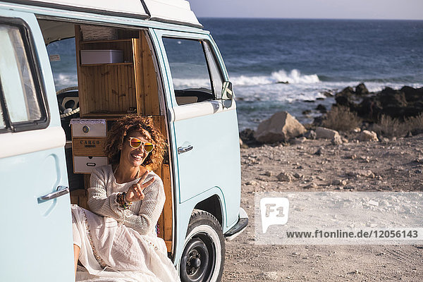 Spain  Tenerife  laughing woman sitting in van parked at seaside showing victory sign