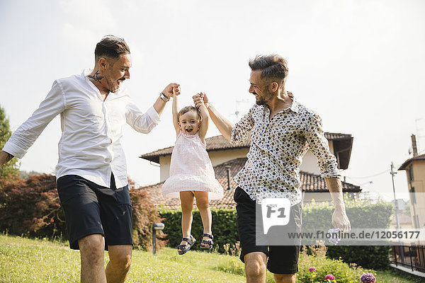 Happy gay couple playing with their child in the garden