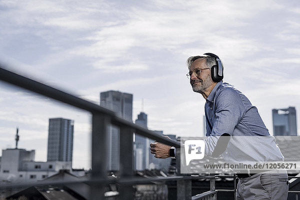 Grauhaariger Mann mit Kopfhörer mit Blick auf die Stadt