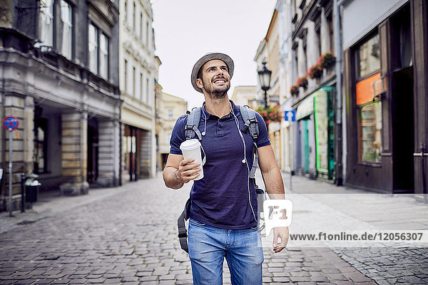 Traveler with backpack walking down city street and holding coffe