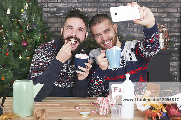 Fröhliches schwules Paar nimmt Selfie mit Smartphone in der Weihnachtszeit mit nach Hause.