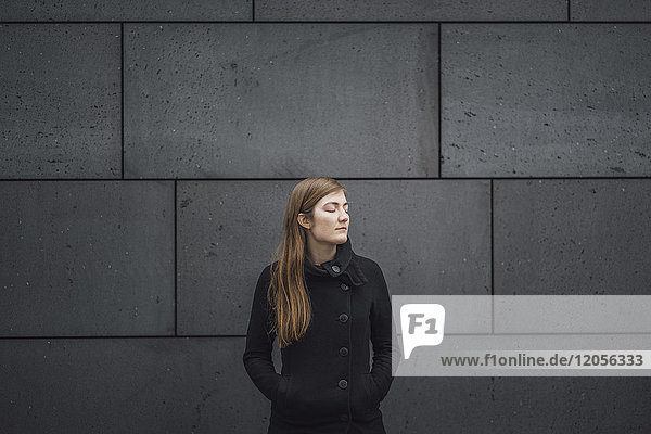 Young woman with eyes closed standing in front of grey facade