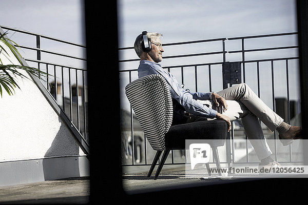 Grauhaariger Mann  der sich auf dem Balkon entspannt und Musik hört