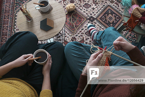 Young couple knitting and having cup of coffee in living room  top view