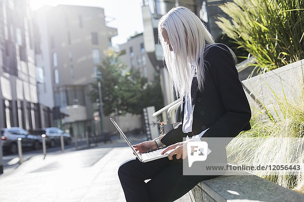 Junge Geschäftsfrau sitzt auf einer Wand in der Stadt mit Laptop