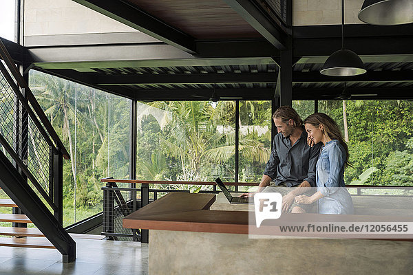 Lächelndes Paar mit Laptop in moderner minimalistischer Küche im zeitgenössischen Designhaus