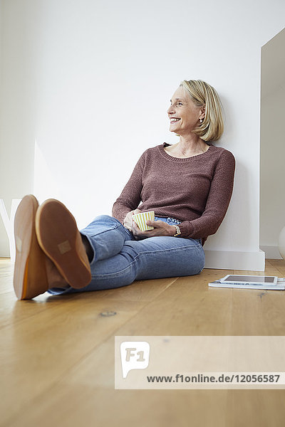Lächelnde reife Frau zu Hause auf dem Boden sitzend