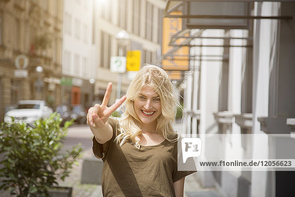Porträt einer glücklichen blonden Frau mit Siegeszeichen