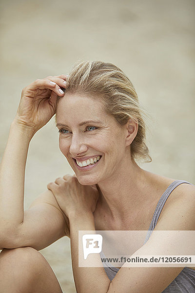 Porträt einer lachenden  blonden Frau  die am Strand sitzt