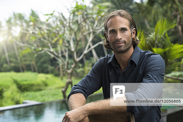 Porträt eines hübschen Mannes vor dem Swimmingpool und dem atemberaubenden tropischen Garten.