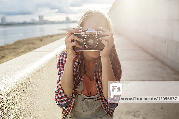 Junge Frau beim Fotografieren mit einer Kamera am Flussufer