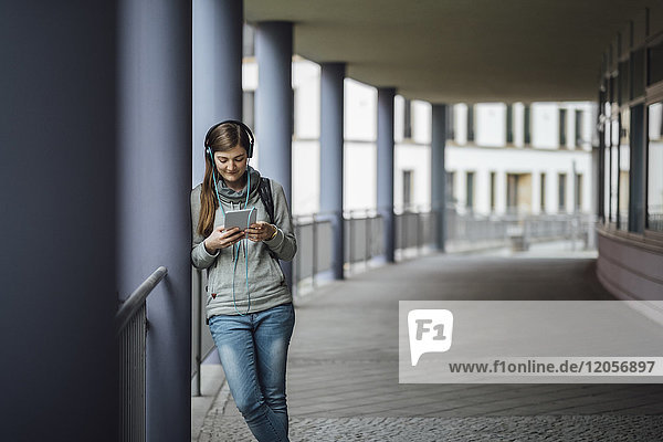 Junge Frau mit Kopfhörer beim Blick auf Mini-Tablett im Freien
