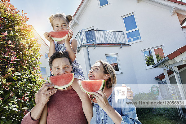 Porträt einer glücklichen Familie mit Wassermelonenscheiben vor dem Haus