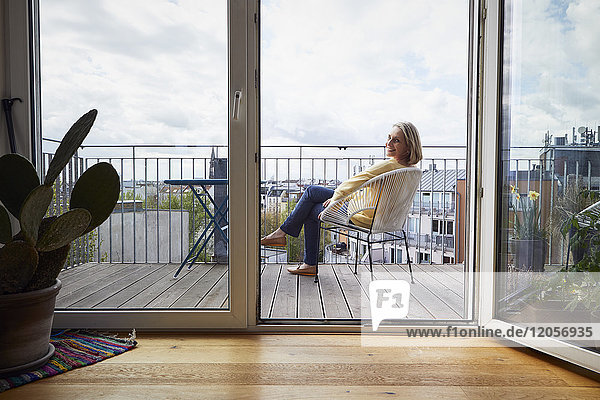Lächelnde reife Frau zu Hause auf dem Balkon sitzend
