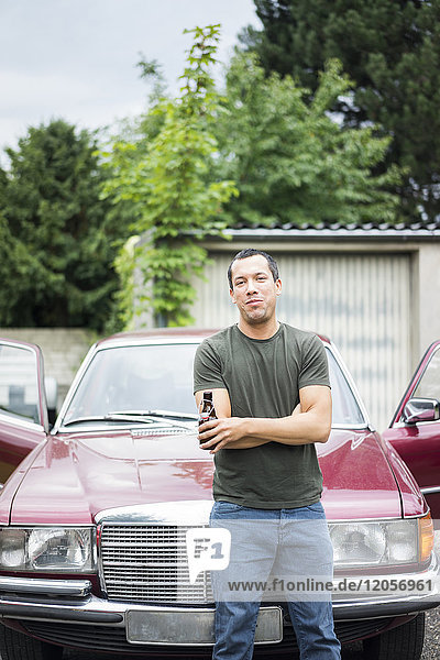 Porträt eines selbstbewussten Mannes mit Bierflasche vor dem Auto stehend