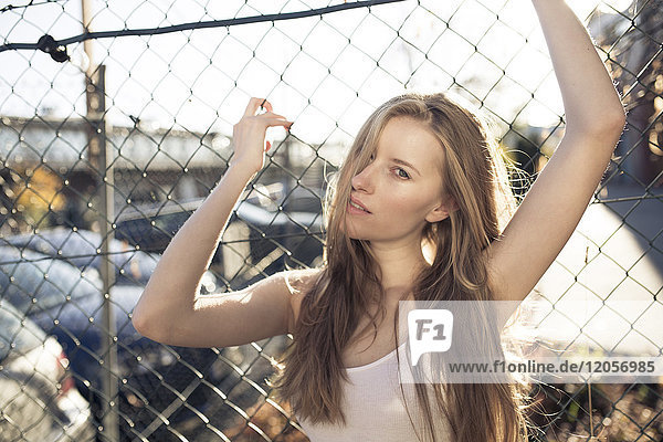 Portrait of young woman in front of wire mesh fence