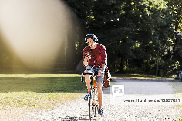 Mann auf Rennrad mit Blick auf Handy im Park