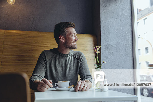 Smiling mature man sitting in cafe looking out of window