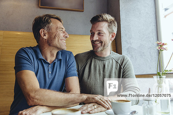 Gay couple putting their hands together with wedding rings in cafe