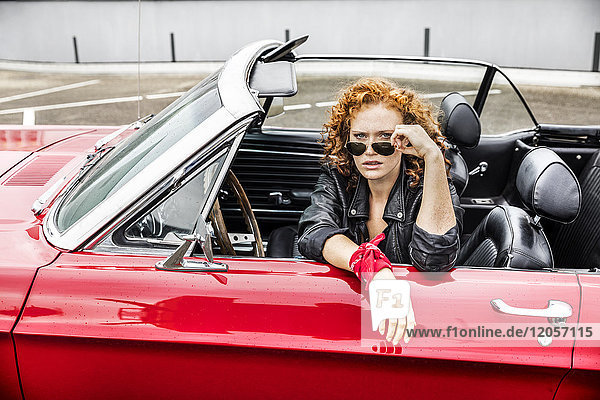 Porträt einer rothaarigen Frau mit Sonnenbrille im Sportwagen