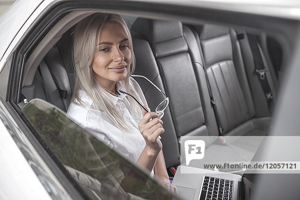 Smiling businesswoman with glasses using laptop in car