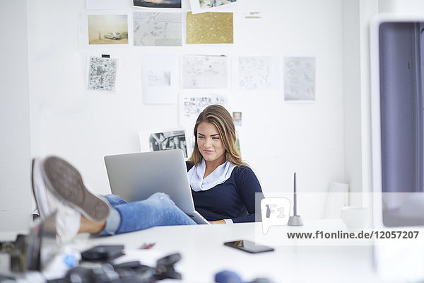 Smiling young woman using laptop at desk in office
