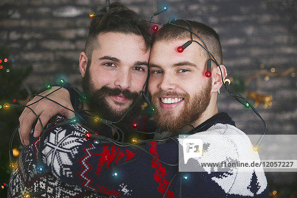 Porträt eines glücklichen schwulen Paares mit Lichterkette zur Weihnachtszeit