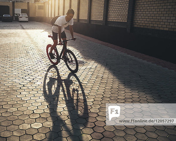 Junger Mann  der bei Sonnenuntergang auf dem Hinterhof Fahrrad fährt.