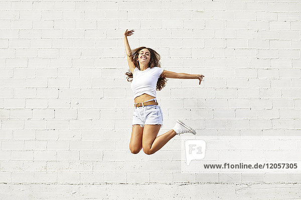 Fröhliche junge Frau springt in der Luft vor weißer Wand
